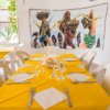 Sala da pranzo con tovaglie gialle e murale artistico.