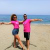 Due persone sorridenti in maglietta rosa sulla spiaggia.