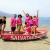 Gruppo in maglietta rosa su una barca rossa in spiaggia.