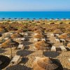Spiaggia con ombrelloni di paglia e lettini fronte mare.