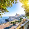 Panorama costiero con edifici storici, mare e alberi al tramonto.