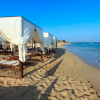Spiaggia sabbiosa con gazebo bianchi e lettini sotto un cielo limpido.