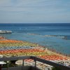 Spiaggia affollata con ombrelloni colorati e mare azzurro.