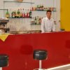 Bancone rosso con bartender e sgabelli neri.