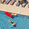 Piscina con persone che nuotano e lettini a bordo.