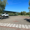 Parcheggio pavimentato con un'auto bianca sotto una tettoia e ulivi intorno.