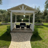 Gazebo bianco con mobili neri, situato su un prato verde con sentiero di pietra.