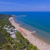 Spiaggia sabbiosa affacciata su un mare azzurro, con ombrelloni e vegetazione circostante.