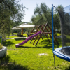 Giardino con trampolino, scivolo viola e tavoli sotto un gazebo.