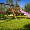 Parco giochi con altalene, scivolo rosa e casetta colorata su erba verde.