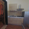 Cucina compatta con mobili in legno, lavello, fornelli, cappa e frigorifero in acciaio.