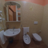 Bagno con lavabo, bidet e wc. Rivestimento mosaico beige e specchio con scaffali.