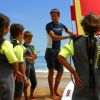 Istruttore parla a bambini in wetsuit vicino a una tavola da surf.