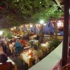Ristorante all'aperto con tavoli illuminati, vegetazione sopraelevata.
