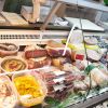 Banco frigo con salumi, formaggi e altri cibi.