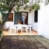 Patio esterno con tavolo, sedie bianche e albero.