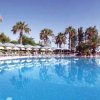 Piscina circondata da palme e ombrelloni bianchi.