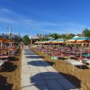 Spiaggia con file di lettini e ombrelloni arancioni e verdi.