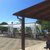 Terrazza con tavoli sotto un gazebo bianco, cielo sereno.