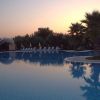 Piscina riflettente al tramonto con palme e lettini.