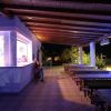 Bar esterno con tavoli in legno, illuminato di sera.