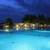 Piscina illuminata di sera con lettini e ombrelloni, cielo blu scuro.