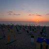 Spiaggia al tramonto con altalena e lettini vuoti.