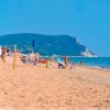 Spiaggia con ombrelloni blu e promontorio sullo sfondo.