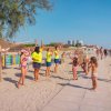 Persone in magliette gialle organizzano attività per bambini su una spiaggia soleggiata.