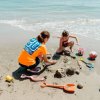 Due persone giocano sulla spiaggia con palette e secchielli.