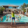 Un istruttore anima un gruppo di persone in piscina durante un'attività di acquagym all'aperto.