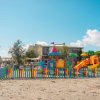 Parco giochi colorato su una spiaggia sabbiosa, circondato da una recinzione.