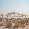 Una spiaggia con ombrelloni beige e lettini di legno su sabbia sotto un cielo sereno.