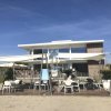 Edificio moderno sulla spiaggia con area esterna arredata e tende ombreggianti.