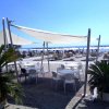 Tavolini con sedie sotto tende bianche sulla spiaggia, con ombrelloni e palme intorno.