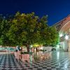 Un cortile con alberi e tavolini all'aperto illuminato di notte.