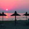 Tramonto su spiaggia con ombrelloni sagomati.