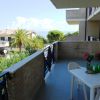 Terrazza con tavolo bianco e sedie, vista mare e vegetazione.