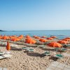 Spiaggia con ombrelloni arancioni e lettini verdi.