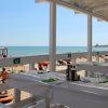 Vista spiaggia con tavoli apparecchiati, mare e bagnanti sullo sfondo.