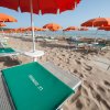 Spiaggia sabbiosa con lettini verdi e ombrelloni arancioni.