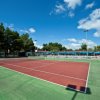Campo da tennis vuoto con un cielo blu e alberi sullo sfondo.