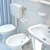 Un bagno con WC, bidet e lavabo bianchi su fondo a righe blu.