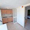 Cucina ad angolo con armadietti in legno e porta aperta verso una stanza.