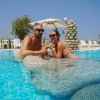 Due persone in una piscina, sorridenti e con occhiali da sole.