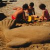 Bambini giocano con una scultura di sabbia a forma di pesce.