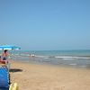 Spiaggia sabbiosa con bagnanti e un ombrellone azzurro.