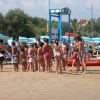 Gruppo di bambini in cerchio sulla spiaggia accanto a un bagnino.