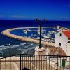 Porto con molo curvo, mare blu e edifici con tetti rossi.
