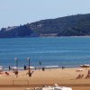 Spiaggia con lettini e ombrelloni, collina sullo sfondo.